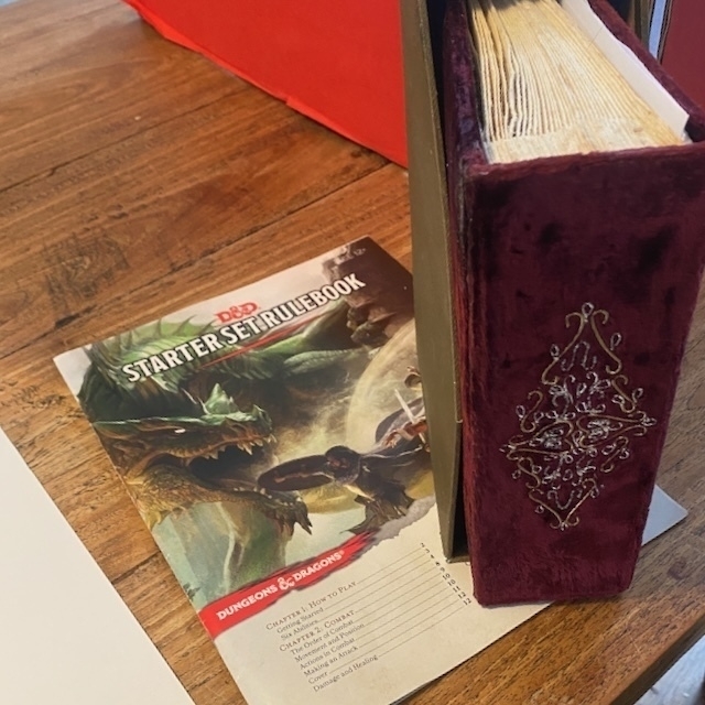 A Dungeons & Dragons starter set rulebook and a velvet-covered book are placed on a wooden table.