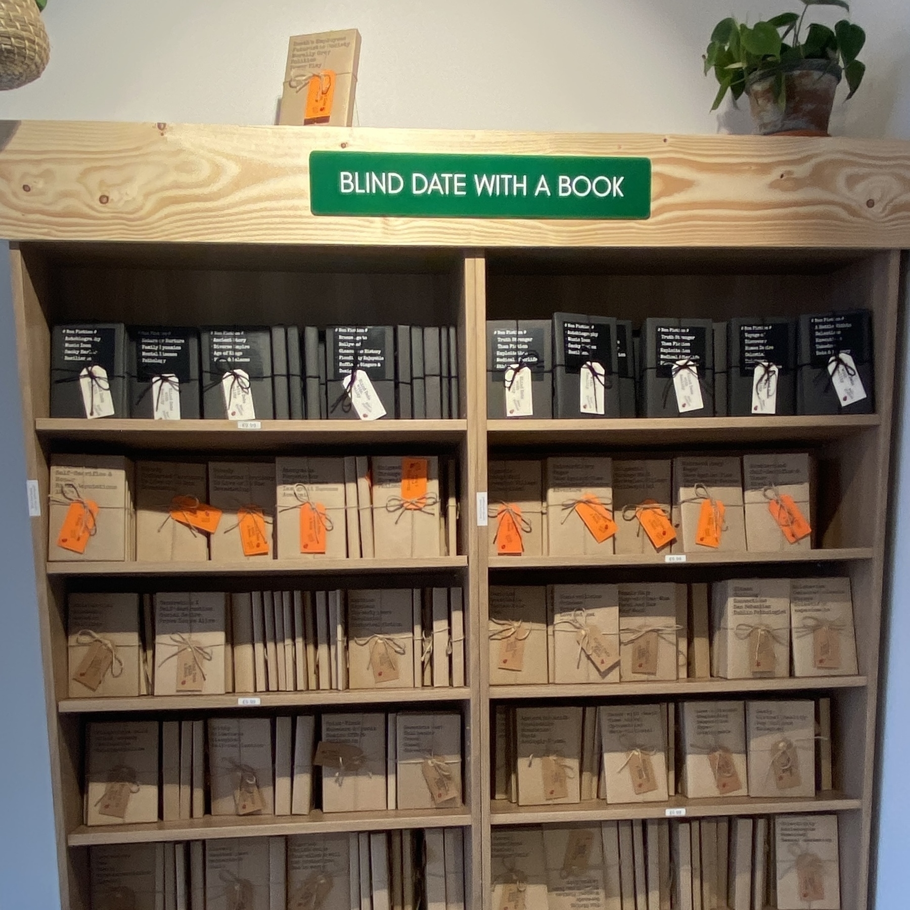 Een blootgestelde boekenkast met ingepakte boeken met labeltjes die labels dragen en een mooi bord met de tekst ‘blind date with a book’ bovenaan de kast.