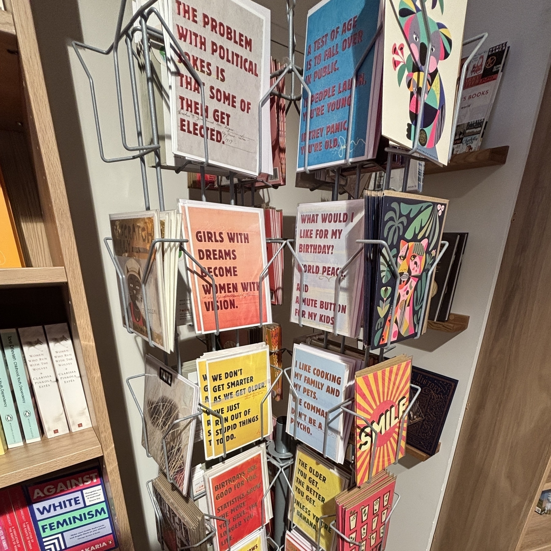 Een standaardhouder met verschillende kleurrijke kaarten staat centraal tekst op de kaarten behandelt thema’s als dromen en verjaardagen de houder bevindt zich in een boekwinkel met boeken op de achtergrond