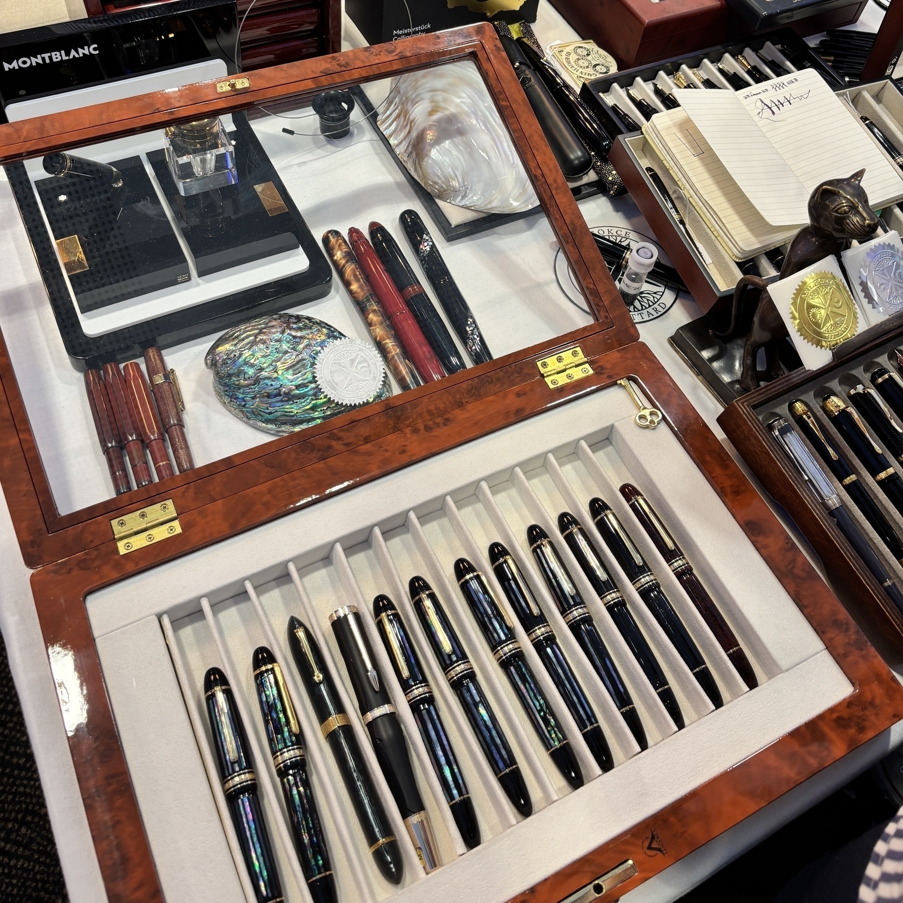 Een elegante verzameling van luxe pennen is uitgestald in een houten doos met glazen deksel.