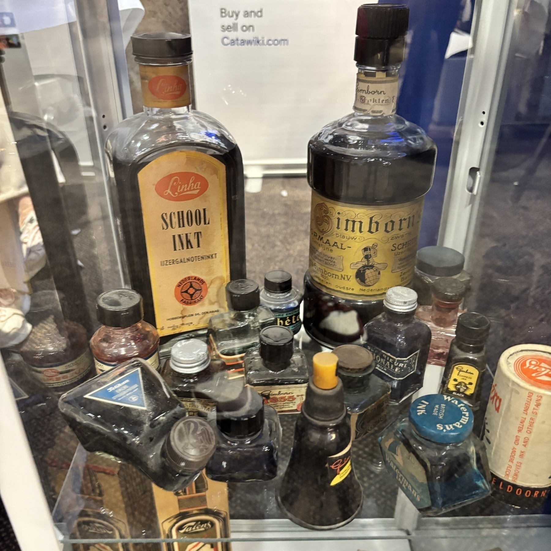 Flessen met verschillende soorten inkt en containers zijn te zien in een glazen vitrine.